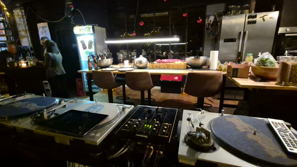 DJ-Pult mit Plattenspielern vor einer offenen Küche in einer urbanen Eventlocation